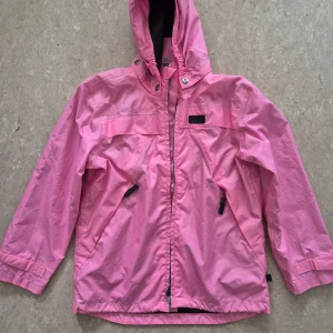 Vindjacka - Snygg rosa vindjacka från Mywear Active med huva och dragkedja framtill. Jackan har två snedställda fickor med dragkedja och coola detaljer med ACTIVE-tryck på insidan. Perfekt för blåsiga dagar och har en sportig vibe. Har några fläckar.