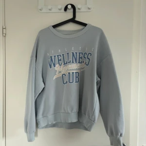 Ljusblå sweatshirt - Sweatshirt i ljusblått med tryck i vitt och blått framtill. Rund hals, ribbade muddar vid ärmslut och nederkant. Oversized passform och långa ärmar. Perfekt för chill dagar eller när du vill ha en sportig vibe.