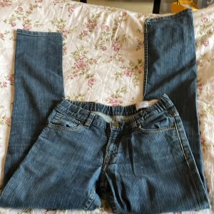 Blå slim jeans Polarn O. Pyret 140 - Snygga blå jeans från Polarn O. Pyret i slim fit-modell. Klassisk femficksdesign, gul kontrastsöm och knapp med logga. Jeansen har normal midja och är tillverkade i mjukt denimtyg som passar perfekt till vardagslooken.