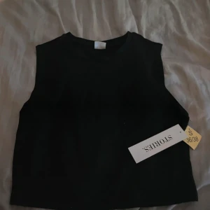 Svart croppad linnetopp från Stories - Säljer en svart croppad linnetopp från Stories i storlek S. Toppen är ärmlös med rund hals och har en stilren, enkel design som är lätt att matcha. Perfekt för dig som gillar minimalistisk stil och vill ha en topp som funkar till många looks.