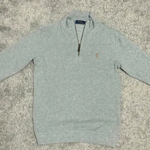 Grå Polo Ralph Lauren Half Zip  - Ljusgrå långärmad half zip i storlek S från Polo Ralph Lauren med klassisk half zip-dragkedja och broderad logga på bröstet. Tröjan har en hög krage och är tillverkad i mjuk bomull, perfekt för lager-på-lager-stil.