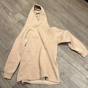 Beige hoodie från 157 XS/S - Mjuk och oversized beige hoodie från 157 med huva och långa ärmar. Insidan är fodrad med fluffig fleece som gör den extra skön och varm. Perfekt för kyliga dagar och har en enkel, clean look som passar till allt.