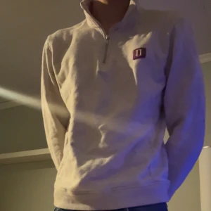 Beige half zip-tröja från les deux - Säljer en beige långärmad tröja från les deux med half zip och ståkrage. Tröjan har ett litet lila HH-märke på bröstet och är tillverkad i mjukt material som passar perfekt för chill dagar. Enkel och clean design.