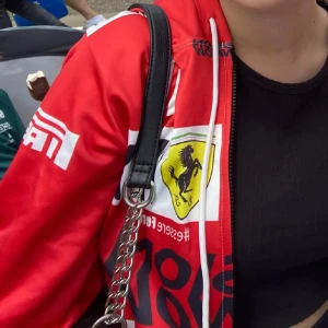 CL 16 fleece - Säljer en röd fleece med vita och svarta detaljer, samt stora tryck och logga på bröstet. Jackan har dragkedja framtill och vit snörning vid huvan. Perfekt för dig som gillar motorsport och vill sticka ut. Har en liten fläck men syns inte särskilt mycket annars helt nytt skick