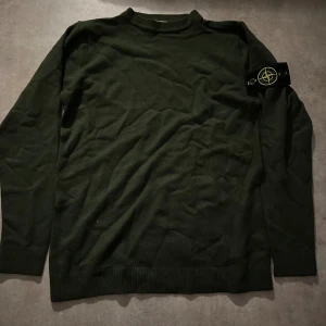 Mörkgrön stickad tröja Stone Island - Snygg mörkgrön stickad tröja från Stone Island med klassisk patch på vänster ärm. Tröjan har rund hals, ribbade muddar och lång ärm. Perfekt för dig som gillar streetwear och vill ha något stilrent med ikonisk logga. Priset går att diskuteras💫