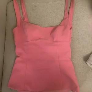 Rosa urringad  topp med öppen rygg och rosett från Zara - Supersnygg rosa topp från Zara med breda axelband och figurnära passform. Toppen har en stor rosett och öppning i ryggen samt dold dragkedja. Materialet är slätt och känns lyxigt. Perfekt för fest men också andra lite spreciellare tillfällen.