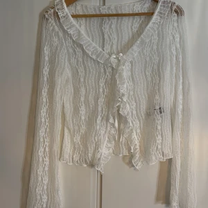 Vit spetsig topp med volang - Jätte fin spetts kofta/topp med lite blommigt mönster och volanger.