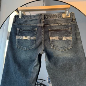 Lågmidjade jeans - Guess - Märke: Guess  Storlek: 28 enligt lapp. Passar bäst någon mellan storlek 36 och 38. Färg: Blå Skick: ✨ Mycket gott skick Passform: Lätt Bootcut Detaljer: Metallogga på bakfickor och en liten på högra framfickan.  Mått:  Innerbenslängd: 78 cm Totallängd: 97 cm Gren: 19 cm Midja rakt över: 39 cm 