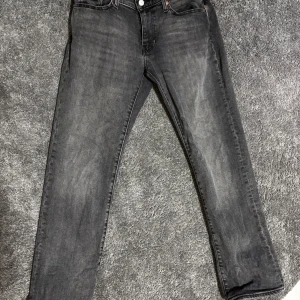 Grå Levi's 514 - Snygga svarta Levi's 514 jeans i klassisk rak modell. Jeansen har fem fickor, silverfärgade nitar och Levi's Premium-märke. Materialet är slitstarkt denim i bomull och passformen är normal med raka ben.