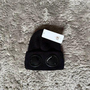 C.P Company mössa  - Stilren mössa från C.P. Company i helsvart – en modern och tidlös accessoar med den ikoniska linsdetaljen framtill. Perfekt för kalla dagar och en clean streetwear-look.  ♦️ One size – stretchig passform ⚜️ Helt nytt skick med tagg ♦️ Premiumkvalitet i mjukt och värmande material  📦 Fraktas inom 24 timmar & trygg affär