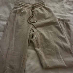 Beige mjukisbyxor med snörning - Säljer ett par beige mjukisbyxor med ribbad midja och snörning i midjan. Byxorna har en avslappnad passform och är gjorda i mjukt material som är perfekt för chill dagar. Metalländar på snöret ger en snygg detalj. Använda 1 gång, från hm