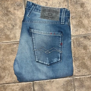 Replay Anbass jeans -  Replay Anbass jeans i blå tvätt med slim passform. Klassisk femficksdesign, coola detaljer på bakfickorna och Replay-märke bak i midjan. Jeansen är gjorda i stretchigt denim för skön komfort och sitter tajt längs benen. Midja 40cm, längd 101cm. JAG SKICKAR EJ FLER BILDER NÄR JAG BÄR JEANSEN! för storleksguide hänvisar jag till måtten och för bättre inblick i passformen rekommenderar jag att googla på modellnamnet. Jeansen kan vara uppsydda utan att jag noterat det så kolla måtten noggrant S4
