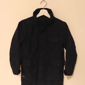 Didriksons vinterjacka - Svart parkas från Didriksons med huva och fuskpäls, flera fickor framtill och broderad logga på bröstet. Jackan har mysigt teddyfoder på insidan och är perfekt för kalla dagar. Klassisk och stilren design som funkar till det mesta.