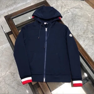 Marinblå hoodie från Moncler - Snygg marinblå hoodie från Moncler med dragkedja, huva och snörning. Ärmsluten har coola detaljer i vitt, rött och svart. Klassisk Moncler-logga på ärmen. Perfekt för dig som gillar stilrena och sportiga plagg.