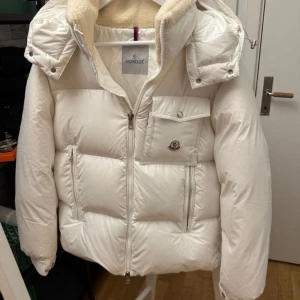 Vit pufferjacka från Moncler - Säljer en snygg vit pufferjacka från Moncler med huva och fluffigt foder. Jackan har dragkedja framtill, fickor med lock och Moncler-logga på bröstet. Perfekt för kalla dagar och har en riktigt clean look. Jag tycker denna jackan är lite speciellt eftersom det inte är många som bär på en vit jacka. Den varm för en kall vinterjacka och helt oanvänd. 2799 är mitt pris men det är inte hugget i sten. Kontakta gärna vid intresse  finns inne alla storlekar 