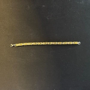 Guldigt kedjearmband med mönster - Snyggt armband i guld- och silverfärgad metall med ett coolt geometriskt kedjemönster. Perfekt för dig som gillar detaljer och vill ha något som sticker ut på handleden. Lätt att ta på med smidig låsanordning.