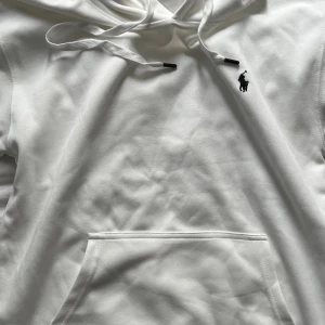 Vit hoodie från Polo Ralph Lauren - Hej!  Säljer en Vit hoodie från Polo Ralph Lauren med klassisk svart broderad logga på bröstet. Tillverkad i mjuk bomull med huva och snörning samt en stor magficka framtill. En stilren och tidlös tröja med riktigt premiumkänsla.  Tröjan är märkt som storlek M men passar bäst för dig som vanligtvis använder storlek S.  Vill du veta något mer eller vill ha fler bilder så är det bara att skriva! Priset är såklart inte hugget i sten!