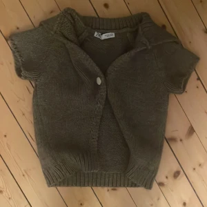 Brun stickad kofta från Zara - Mysig brun stickad kofta från Zara med korta ärmar och en knapp framtill. Perfekt för lager-på-lager och har en ribbad kant vid midjan. Enkel och chill stil som funkar till jeans eller kjol.