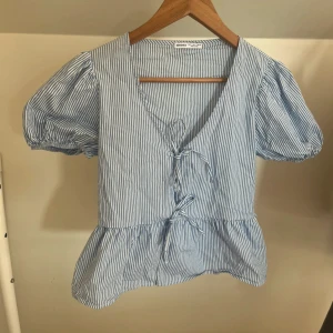 Blårandig blus med snörning från Bershka - Supersöt blus från Bershka i blått och vitt med smala ränder. Modellen har puffiga korta ärmar, v-ringning och snörning framtill. Volangkant nedtill ger en extra girly vibe. 