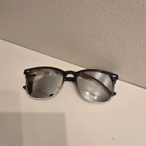 Svarta och silvriga solglasögon - Snygga solglasögon med svart båge upptill och transparent nedtill. Spegelblanka silvriga glas ger en cool look. Klassisk form som passar de flesta ansikten. Perfekta för att lyfta din stil i sommar.