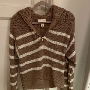 Randig stickad hoodie från Gina Tricot - Mysig stickad hoodie från Monki i beige och vitt med breda ränder. Tröjan har en half zip-dragkedja framtill, huva och långa ärmar. Perfekt för lager på lager och chill dagar.