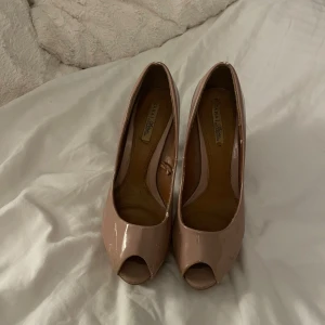 Beiga platåpumps från Zara - Snygga pumps från Zara i beige lack med hög klack och platåsula. Skorna har öppen tå och rundad form framtill, vilket ger en trendig och elegant look. Perfekta för dig som vill sticka ut med stilrena och höga klackar.
