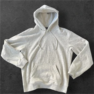 Grå hoodie från H&M  - Säljer en stilren grå hoodie från H&M i loose fit. Tröjan har huva med snörning, magficka och långa ärmar med ribbade muddar. Perfekt för chill dagar eller när du vill ha en enkel och clean look. Nästan aldrig använd