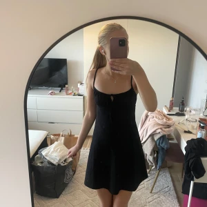 Svart kort klänning från Gina Tricot - Supersöt svart kort klänning från Gina Tricot i storlek XXS. Klänningen har tunna axelband, lätt utställd passform och en liten knytning framtill vid bysten. Materialet är strukturerat och känns mjukt mot huden. Perfekt för varma dagar och snygg att styla med smycken.