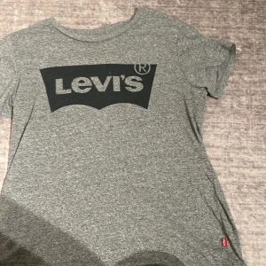 Grå Levi's t-shirt med logga - Snygg grå t-shirt från Levi's med stor svart logga framtill. Klassisk rund halsringning och korta ärmar. Tillverkad i mjuk bomull för en skön känsla. Perfekt för en avslappnad och stilren look.