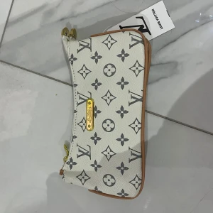  kuvertväska  - Snygg vit kuvertväska med klassiskt monogrammönster i svart och detaljer i guld.  Perfekt för dig som vill ha en ikonisk accessoar med lyxig känsla.
