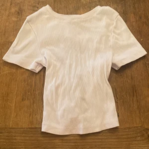 Vit ribbad topp med snörning i ryggen - Säljer en vit ribbad topp med kort ärm och snygg snörningsdetalj i ryggen. Toppen har en tight passform och är tillverkad i stretchigt material som sitter skönt. Perfekt för dig som vill ha en basic topp med en twist.