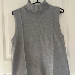 Grå stickad väst med polokrage - Snygg grå stickad väst med hög ribbad polokrage. Västen är ärmlös och har en rak, något loose passform. Den är sparsamt använd!🩷
