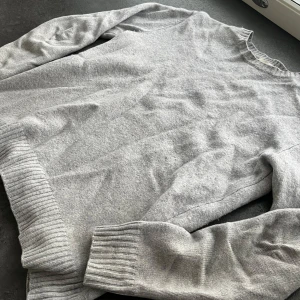 Kashmir tröja John Henric  - En stilren ljusgrå stickad tröja från John Henric i storlek M. Tröjan har rund halsringning, ribbade muddar vid ärmslut och nederkant samt lång ärm. Tröjan är i väldigt bra skick!