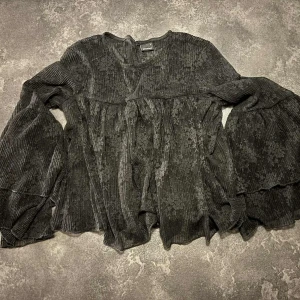 Svart blus med vida ärmar - Supersnygg svart blus i spets med diskret blommönster. Blusen har vida, långa ärmar och en lös, flowy passform. Perfekt för dig som gillar löst sittande kläder.