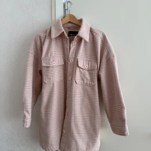 Overshirt i rosa - Superfin rutig overshirt i ljusrosa toner från Pieces. Jackan har knappar framtill, två stora bröstfickor och ett bälte i midjan.. 