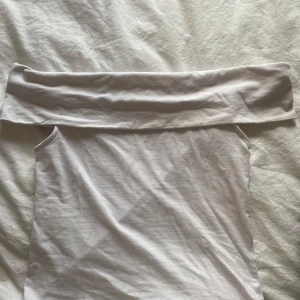 Vit offshoulder topp från Stories XS - Säljer en vit offshoulder topp från  Stories i storlek XS. Toppen är ärmlös med bred kant över axlarna och har en clean, minimalistisk look. Perfekt att styla med jeans eller kjol för en fräsch vibe.