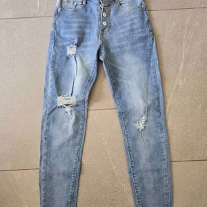 Ljusblå skinny jeans med slitningar - Snygga ljusblå skinny jeans med slitna detaljer på båda benen och knappar i gylfen. Jeansen har klassisk femficksdesign och är perfekta för en avslappnad streetstil.