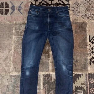 Mörkblå jeans från Nudie Jeans - Jeansen är modellen pipe led och är  w29 l34. På bilden har jag vikt upp jeans kanten för att de ska sitta bättre på mig och det är så jag oftast bär dem. Är 173 och väger 56. De har ett litet håll i högre ficka, skriv vid minsta lilla fråga!