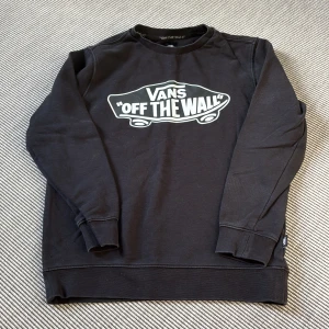 Vans - Svart junior sweatshirt från Vans Off The Wall - Svart sweatshirt från Vans (junior)  med stort 'Off The Wall'-tryck på bröstet. Klassisk rund halsringning och långa ärmar. Mjuk insida och ribbade muddar vid ärmslut och nederkant. Perfekt för en avslappnad streetstyle-look.