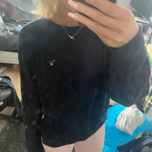 Svart ribbad stickad tröja från GANT - Svart ribbstickad tröja från GANT med broderad logga på bröstet. Klassisk rund halsringning och långa ärmar. Den är i storlek 170 men passar mig som har Xs/S