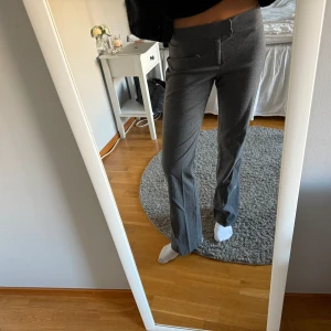 Grå kostymbyxor med bootcut - Snygga grå kostymbyxor med bootcut och klassisk passform. Byxorna har medel midja och raka ben som släpper ut lite nertill. Perfekta för en clean och stilren look. Materialet känns mjukt och följsamt, och färgen är en mörkgrå ton. Som de syns på bilden är de lite noppriga, jag är ca 1.70 cm🩶