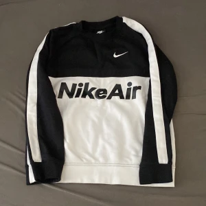 Nike Air svartvit sweatshirt L - Svart och vit sweatshirt från Nike Air med stor logga framtill och broderad Nike Air-detalj på bröstet. Tröjan har långa ärmar med vita ränder längs sidorna och är tillverkad i mjuk bomullsmix. Perfekt för en sportig och avslappnad stil.