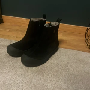 Svarta boots med foder från Canada Snow - Svarta boots från Canada Snow med matt finish och robust gummisula. Skorna har ett varmt, ljust foder på insidan och dragflik baktill för enkel påtagning. Perfekta för kalla och blöta dagar med sin vattentäta design och stilrena look. Aldrig använda.