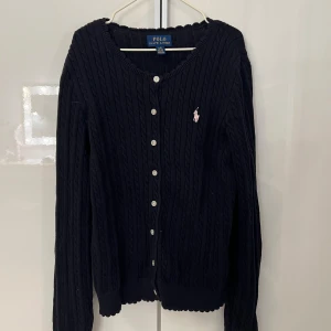 Svart kofta från Polo Ralph Lauren - Säljer en mörkblå kofta från Polo Ralph Lauren med rosa märke/häst. Koftan är i storlek 12-14 år / L i barn storlek. Den är knappast använd och i mycket bra skick.