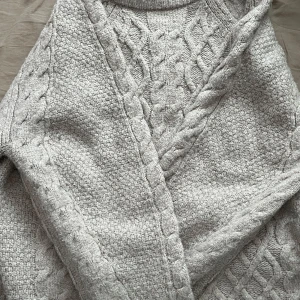 Ljusgrå stickad tröja från 157 - Mysig beiche stickad tröja från 157 med flätstickat mönster framtill och längs ärmarna. Tröjan är mysig nu till vintern. Den är lite stor i storleken 