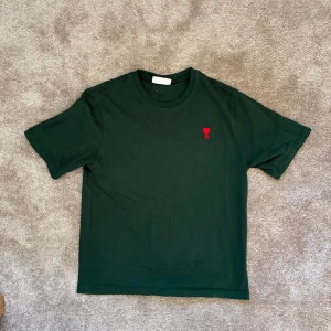 Grön t-shirt från Ami Paris - Snygg mörkgrön t-shirt från Ami Paris med klassisk passform och korta ärmar. Tillverkad i mjuk bomull. Skriv vid frågor eller funderingar✌️