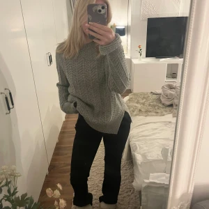 Grå stickad oversized tröja - Mysig grå stickad tröja med grovt mönster och rund hals. Tröjan har en oversized passform och långa ärmar, perfekt för kyliga dagar. Ribbstickade muddar vid ärmslut och nederkant ger en extra snygg detalj.