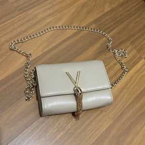Beige axelväska med kedja - Snygg beige Valentino axelväska med guldfärgad kedja. Perfekt för att ge en elegant touch till din outfit. Lite rostig ej äkta 