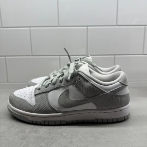 Nike Dunk Low vit/grå manchester - Nike Dunk Low sneakers i vitt och ljusgrått med snygga detaljer i manchestertyg. Skorna är i bra skick inga skador. Använd fåtal gånger.