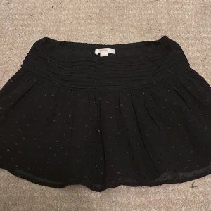 Svart glittrig kortkjol från Gina Tricot - Supersöt svart kortkjol från Gina Tricot med glittriga detaljer och veckad midja. Kjolen har ett flowigt fall och små glittrande prickar över hela tyget som ger en extra touch. Perfekt för dig som vill sticka ut lite extra.